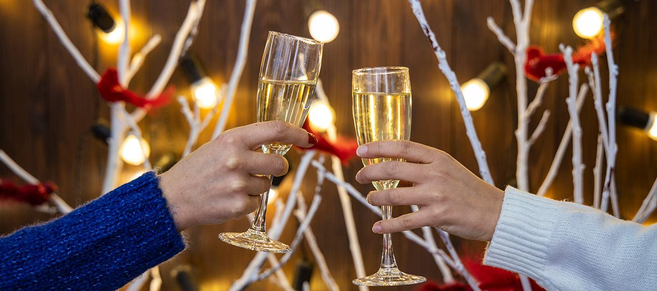 A close up of two glasses in a toast -against a festive backdrop